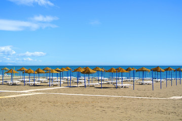 Summer holiday view of a Mediterranean beach prepared for a tourist season, a sandy beach by the blue sea, deckchairs, straw umbrellas and a wooden path at Torremolinos resort on Costa del Sol, Spain.