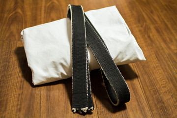 Black belt and Gi for martial arts ( Karate, Judo, Jiu-Jitsu, Kenpo, Taekwondo, Budo) on the wood...