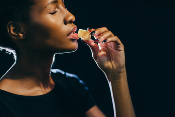 Better than sex, sweets, stress relief, little joy of life concept. A black woman eats white chocolate with pleasure on dark background.
