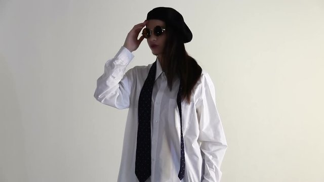 A Young woman in shirt, sunglasses and beret posing on the white background