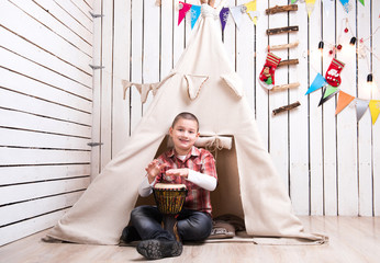 boy sitting on the floor and playing drum near wigwam in decorated wooden room © Ievgen Skrypko
