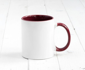 simple white cup with dark red inside and handle on a planked table