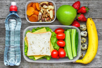Healthy lunch boxes with sandwich, eggs and fresh vegetables, bottle of water, nuts and fruits