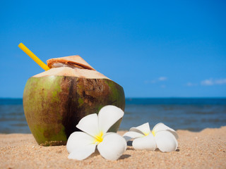 Fresh coconut and plumeria flower on the beach.