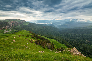 Naklejka na ściany i meble View on mountain forests and distant valley covered with glowing clouds and mist at sunset. Lagonaki, Caucasus, Russia