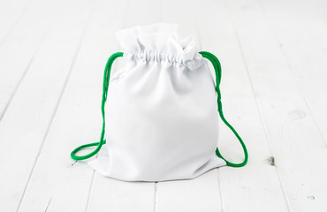 full white fabric gift bag with green ties on wooden table