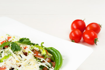 Traditional classic Shopska salad with tomatoes, peppers, cucumbers and cheese in white dish on white wooden table. Bulgarian cuisine, Balkan culture