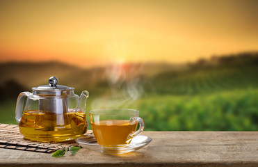 Warm cup of tea and glass jugs or jars and tea leaf on wooden table with the tea plantations...
