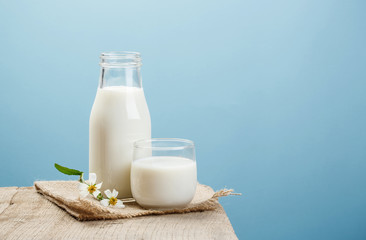 A bottle of milk and glass of milk on a wooden table on a blue background - obrazy, fototapety, plakaty
