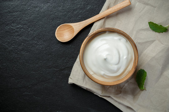 Greek yogurt in a wooden bowl with spoons on stone background