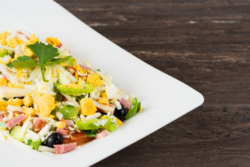 Traditional Bulgarian Shepherd salad with tomatoes, peppers, cucumbers, mushrooms, ham, cheese and eggs in white dish on grey wooden table. Bulgarian cuisine, Balkan culture