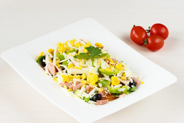 Traditional Bulgarian Shepherd salad with tomatoes, peppers, cucumbers, mushrooms, ham, cheese and eggs in white dish on white wooden table. Bulgarian cuisine, Balkan culture