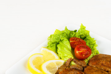Pork fillet steak with cherry tomatoes, lemon and a lettuce in white dish on white background