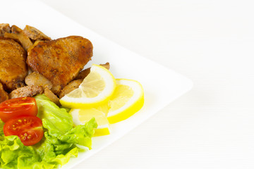 Pork fillet steak with cherry tomatoes, lemon and a lettuce in white dish on white background