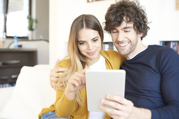 Enjoy browsing on the internet together. Shot of a lovely young couple relaxing at home and using digital tablet. 