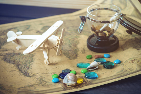 Toy wooden plane on a world map with colored stones and shells from the sea in a retro style.