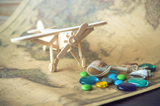 Toy wooden plane on a world map with colored stones and shells from the sea in a retro style.