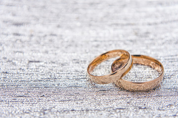 Two golden wedding rings on diamond shiny plate.
