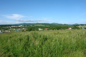 summer grassy meadow with a village and hills in the background