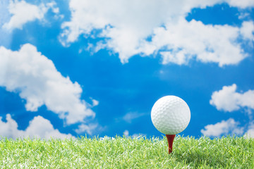golf ball on red tee on green fake grass against sunny cloud and blue sky background