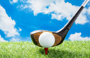 golf ball on red tee with driver against green fake grass and cloud and blue sky background