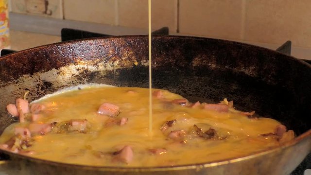 Roasted sausages and onions pouring the egg mixture in the pan to cook. 50 fps