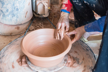 Close-up female hands throwing pottery on the wheel in a clay studio at ceramic village in Vietnam. Hand making, forming clay pot on pottery plate. Artisan making traditional ceramic manually.