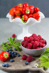 Fresh organic summer berries - ripe raspberry, strawberry, blueberry with leaves on wood background