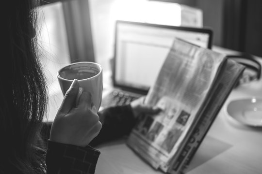 Black and white image a business woman reading newspaper and drinking coffee in the morning in office