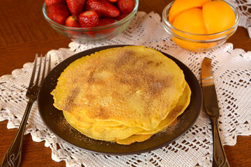 Stack of sweet pancakes with cinnamon decorated on a brown plate on a wooden table.