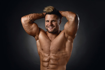 Studio portrait of topless muscular sportsman smiling over black background