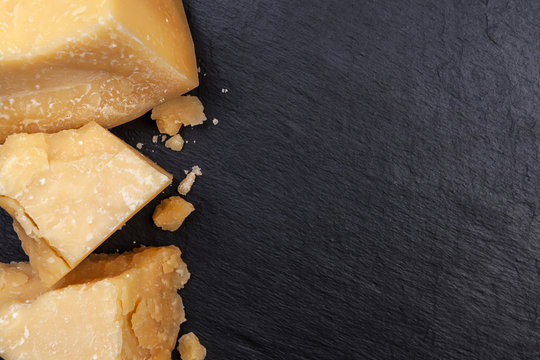 Parmesan cheese on black stone background. Top view, copy space.