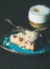 Dessert and coffee. Piece of lemon, ricotta, almond and raspberry gluten-free cake and glass of latte over dark wooden background, selective focus, vertical composition