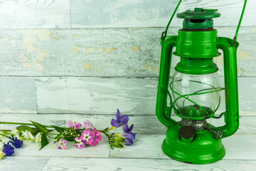Old green lantern with colorful flowers on a rustic white wooden background