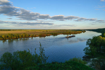 Spring landscape with a view of the bend in the river and a cargo barge