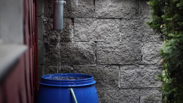 Outlet from the gutter into blue barrel in heavy rain, double slow motion. Eaves in a private house. To save rainwater for the drought. 