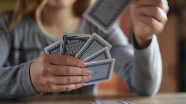 2 teenagers, boy and girl, play cards on a wooden table