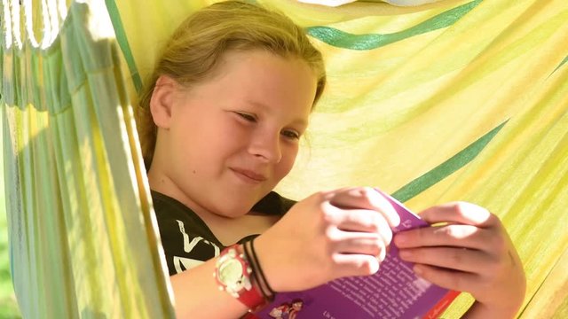Teenager reads a book in her hammock in the summer sun