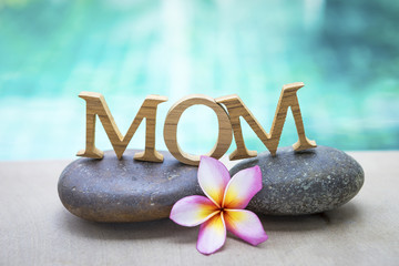 Mother's day concept background, mom wooden text on spa stone with space on blurred swimming pool...
