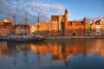 Fototapeta na wymiar Caravel moored by Long Embankment on Motlawa River in the Old Town of Gdansk, Poland at sunrise. Mariacka Gate on the right