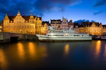 Fototapeta na wymiar Ship moored by Long Embankment on Motlawa River in the Old Town of Gdansk, Poland at night. Illuminated Green Gate on the left
