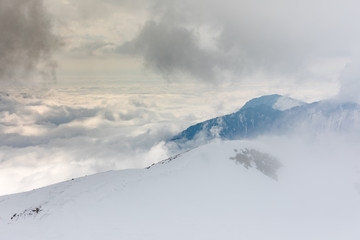 Fototapeta na wymiar Mountain slope with snow in the clouds with focus on the sky