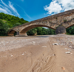 Old stone bridge across the shallow dried at summer river with sand banks