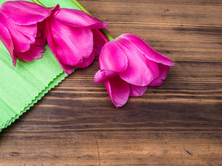 Pink tulips, floral arrangement on wooden background with green paper and space for message. Background for Mother's Day, 8 March and other greeting cards or invitations for lovely women. Soft focus.