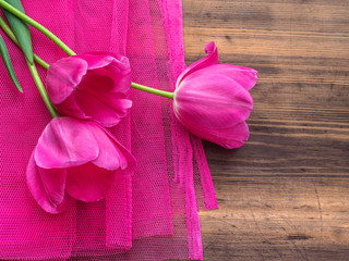 Pink tulips, floral arrangement on wooden background with pink mesh and space for message. Background for Mother's Day, 8 March and other greeting cards or invitations for lovely women. Soft focus.
