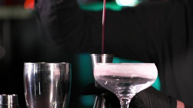 Bartender pours alcoholic drink into small glasses on bar