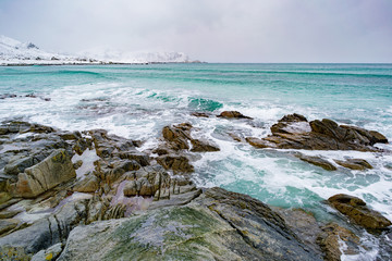 Sunrise on the stone shore of the ocean and mountains with snow on the horizon