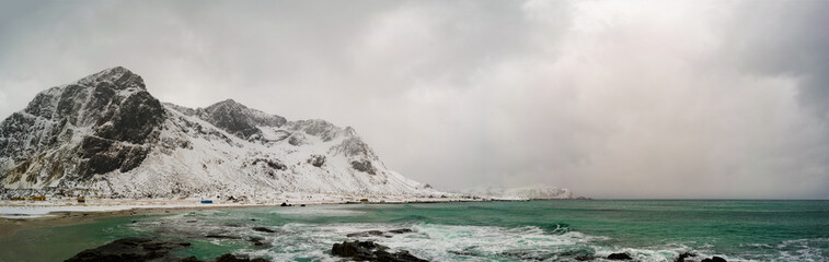 Sunrise on the stone shore of the ocean and mountains with snow on the horizon