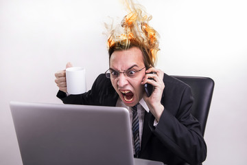 Angry and frustraded business man talking on a cell phone and screaming on his laptop in the...