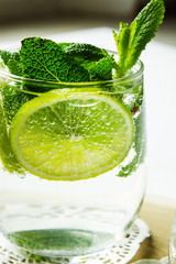 Cold pure carbonated water with lime in a glass on a light background. Selective focus. Vertical.